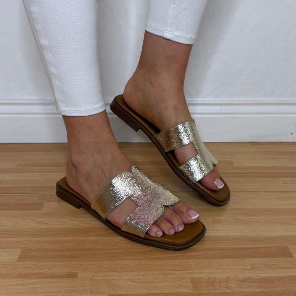 Oh My Sandals 5580 Gold sandals worn with white pants on a wooden floor.