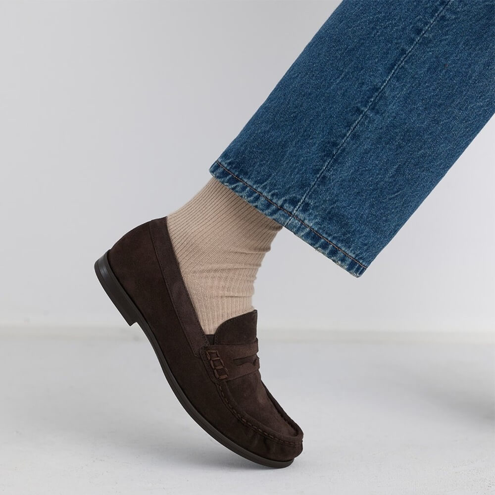 Paul Green Brown loafers worn with beige socks and blue jeans on a light grey background