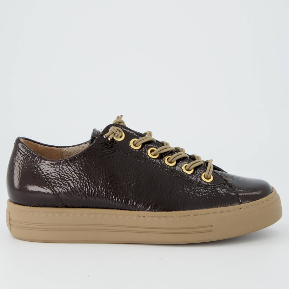 A Paul Green low-top sneaker in glossy dark brown textured leather with beige laces threaded through gold-tone eyelets and a thick beige rubber sole, shown on a light grey background.
