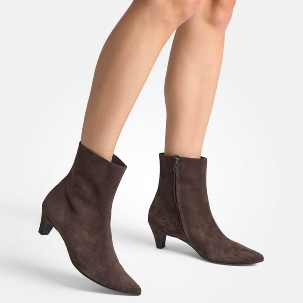 Brown suede ankle boots worn by a person on a light gray background