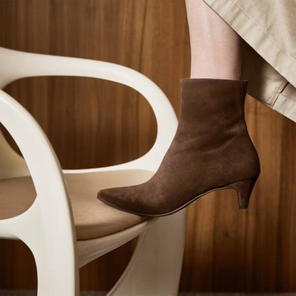 Brown suede ankle boot on a white chair with a wooden background