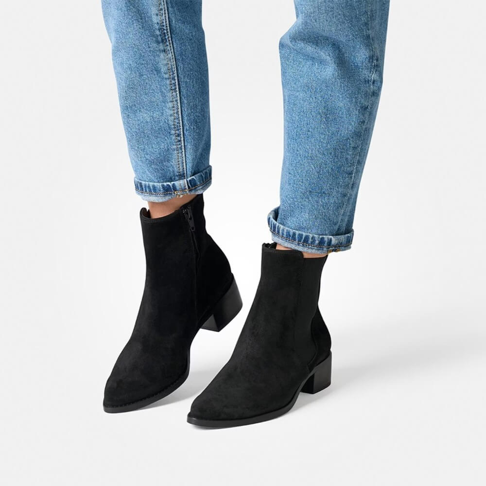 Black ankle boots worn with blue jeans on a white background