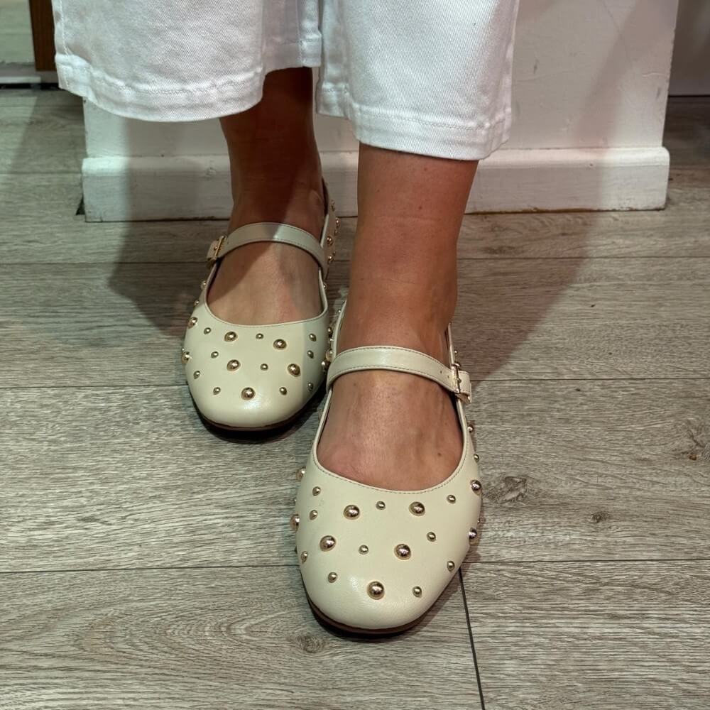 Pedro Anton Beige studded flats worn with light-coloured pants on a wooden floor.