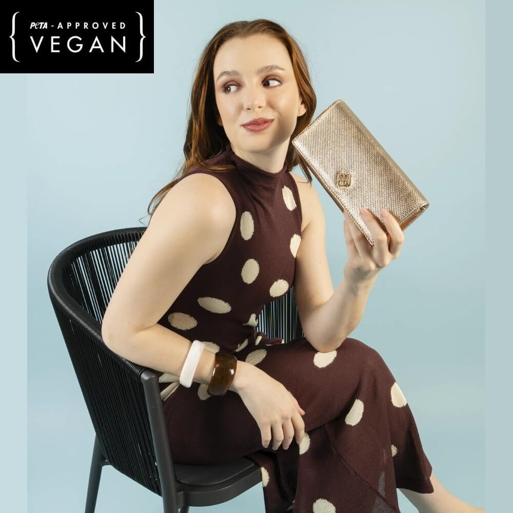 Woman holding a Pepe Moll gold clutch with a blue background and 'PETA-Approved Vegan' label.