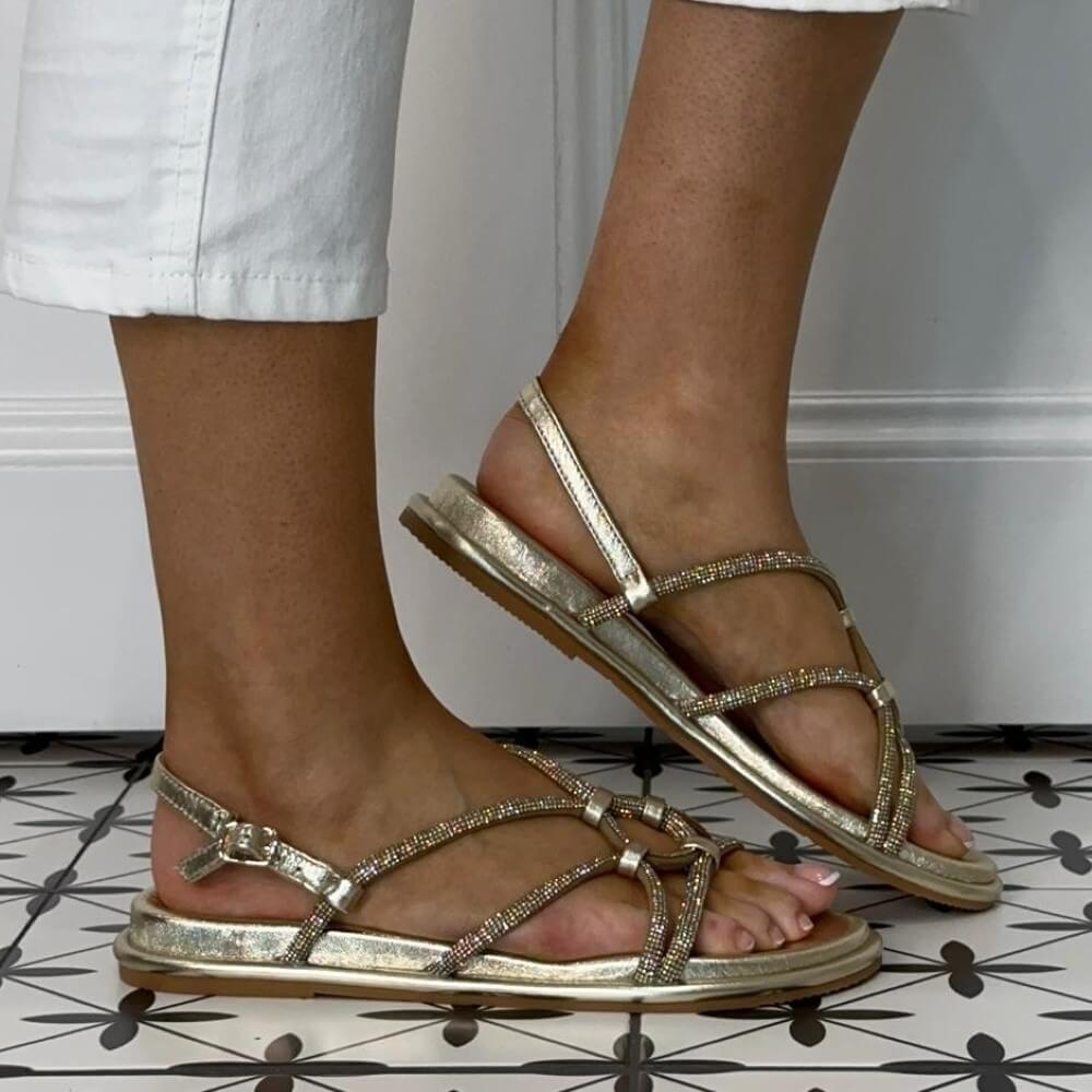 Repo Gold strappy sandals worn with white pants on a tiled floor.