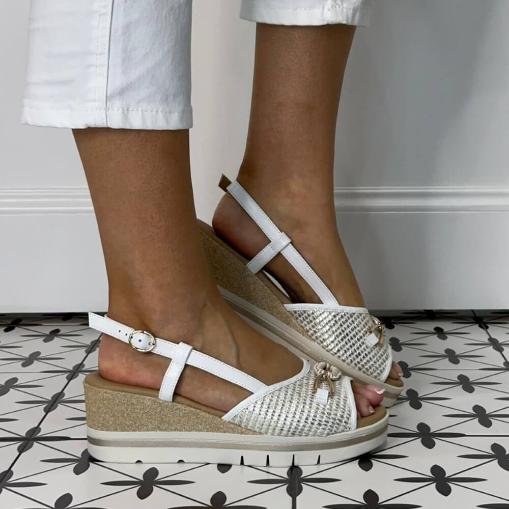 Repo White wedge sandals with gold accents worn by a person on a patterned floor.