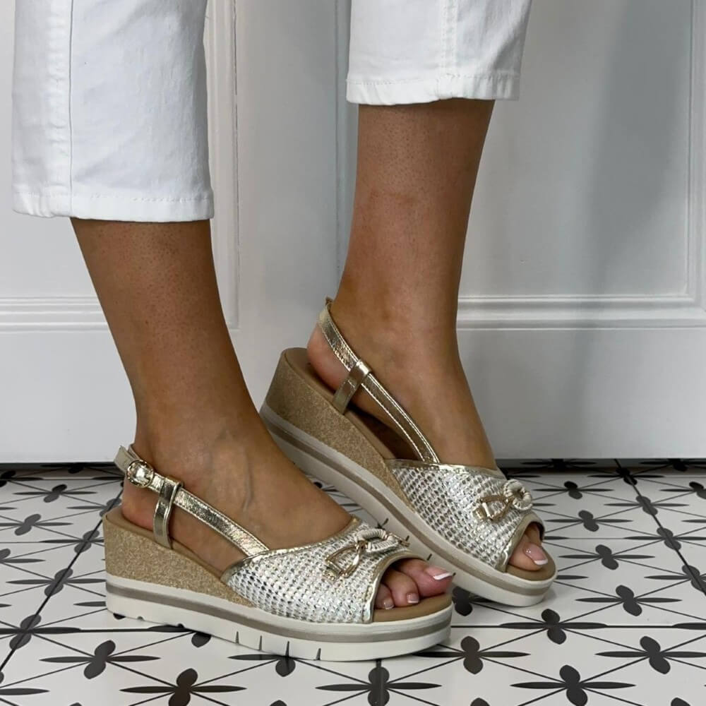Repo Gold wedge sandals worn with white pants on a patterned floor.