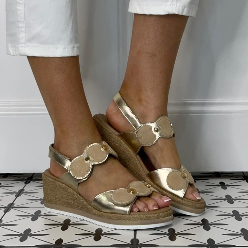 Repo Gold wedge sandals worn with white pants on a patterned floor.