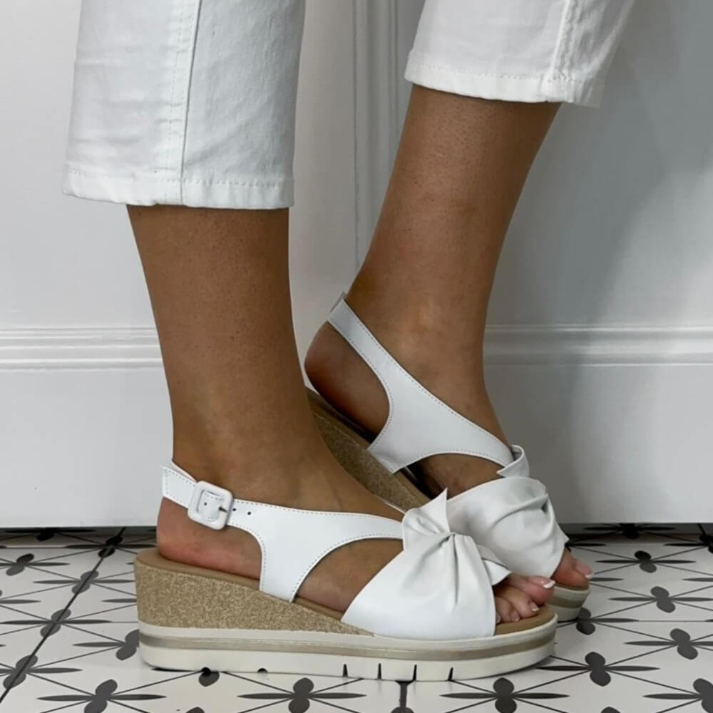 Repo White sandals with a wedge sole worn by a person on a patterned floor.