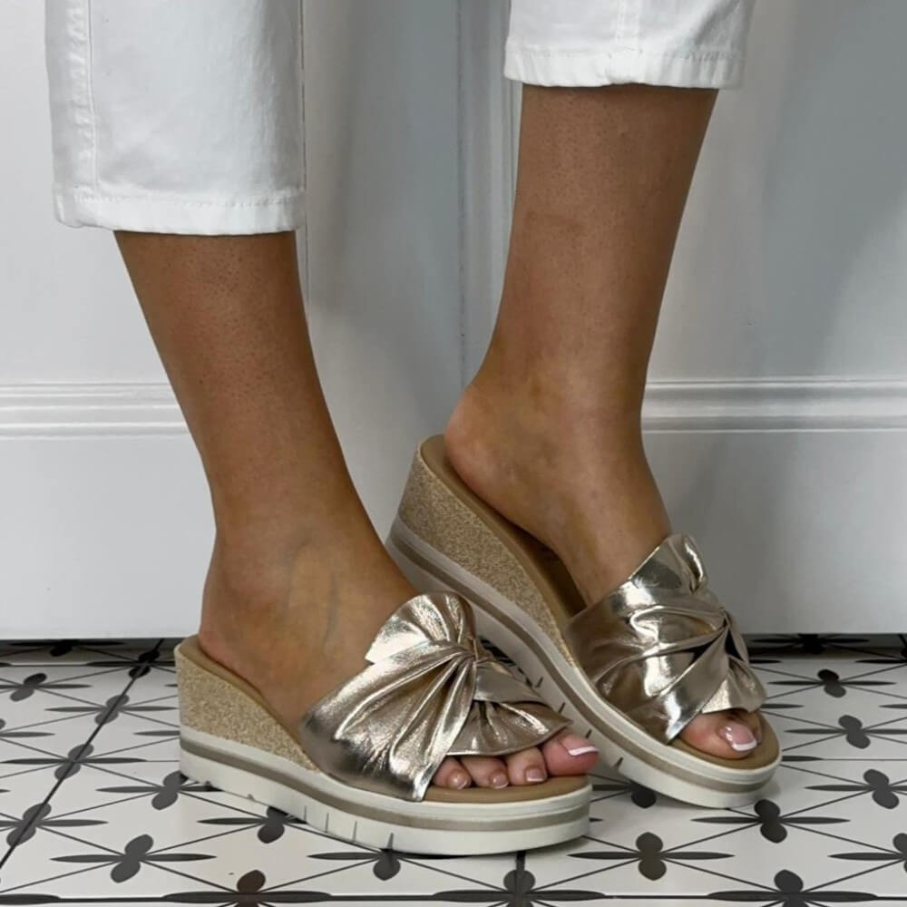 Repo Gold leather sandals with bow detail worn by a person on a tiled floor.