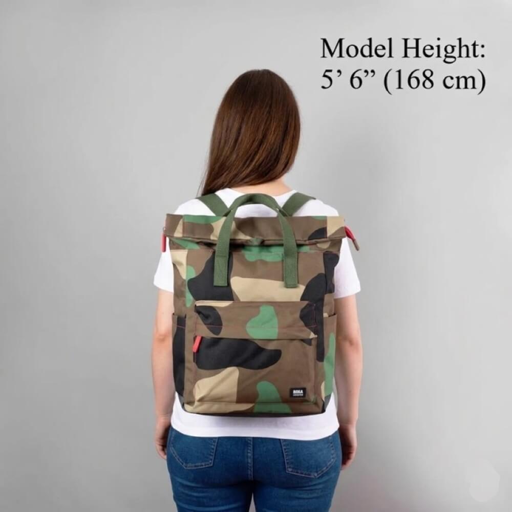 Person wearing a camouflage Roka backpack with model height information on a grey background