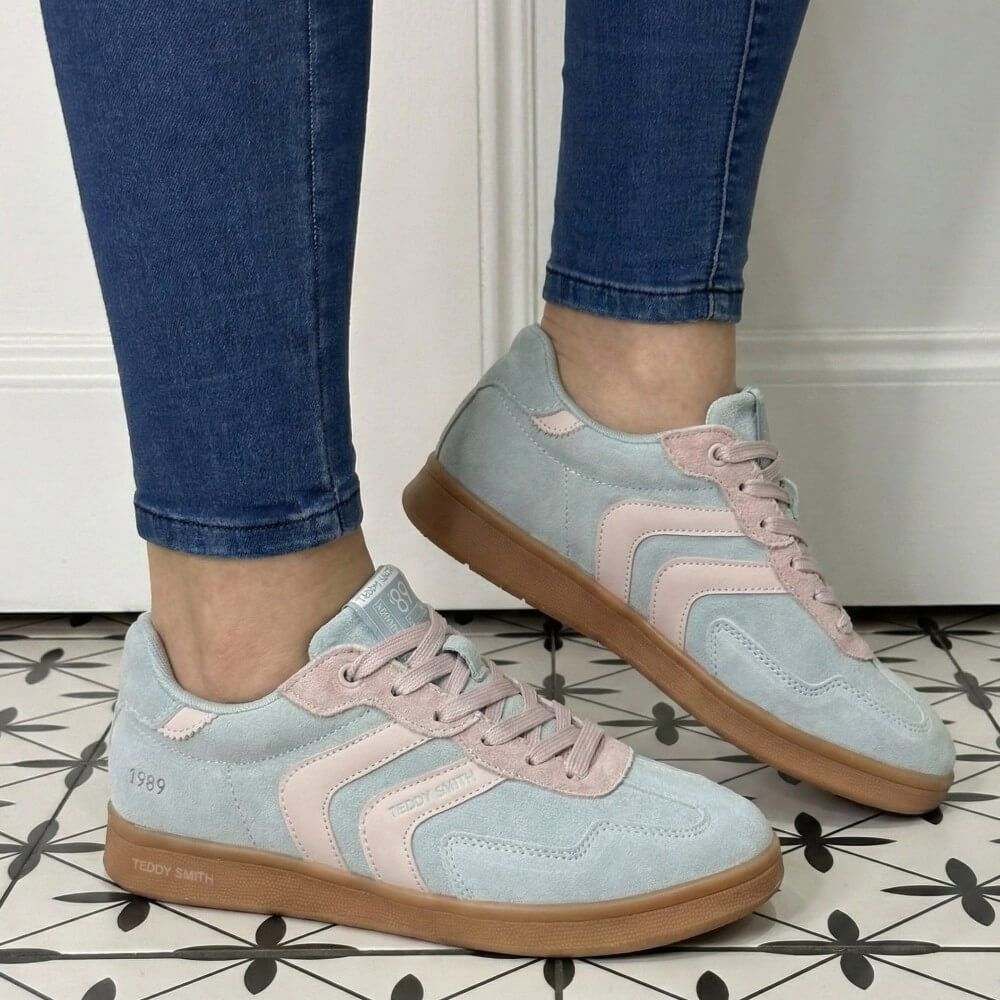 Light blue and pink sneakers with brown soles worn indoors on a patterned floor.