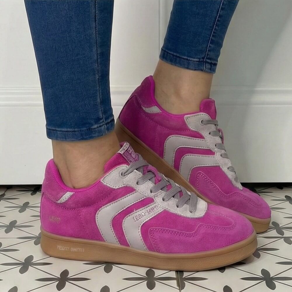 Pink and gray sneakers worn with blue jeans on a patterned floor.