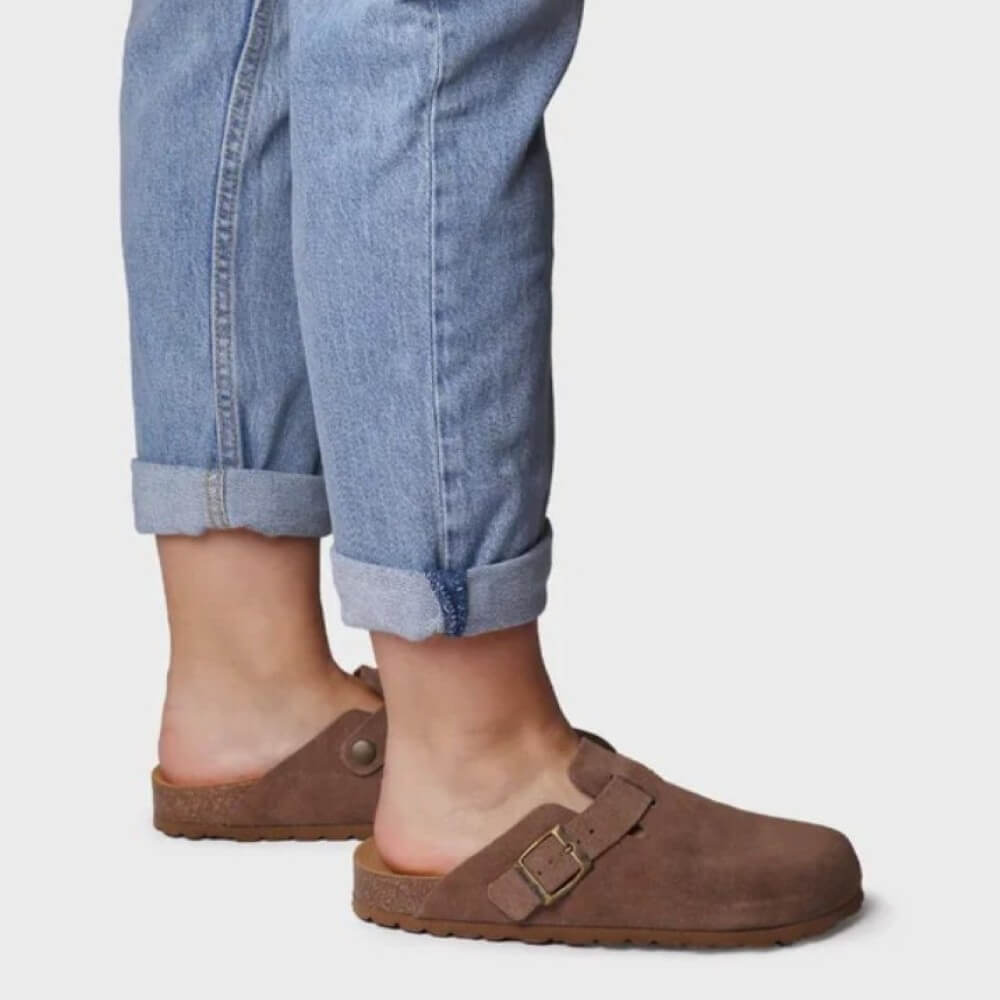 Brown clogs worn with rolled-up blue jeans on a light gray background