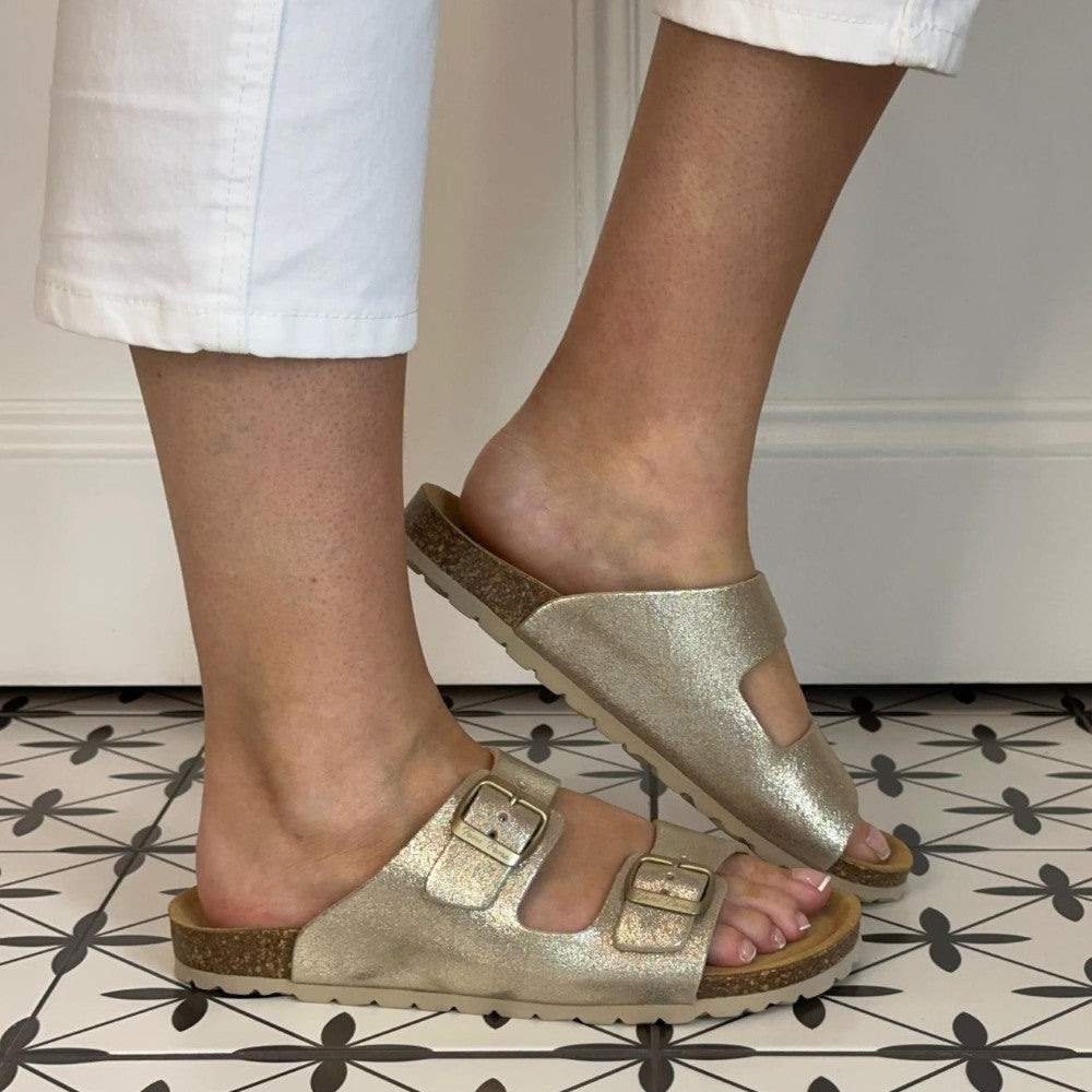 Toni Pons Gold sandals worn with white pants on a patterned floor.
