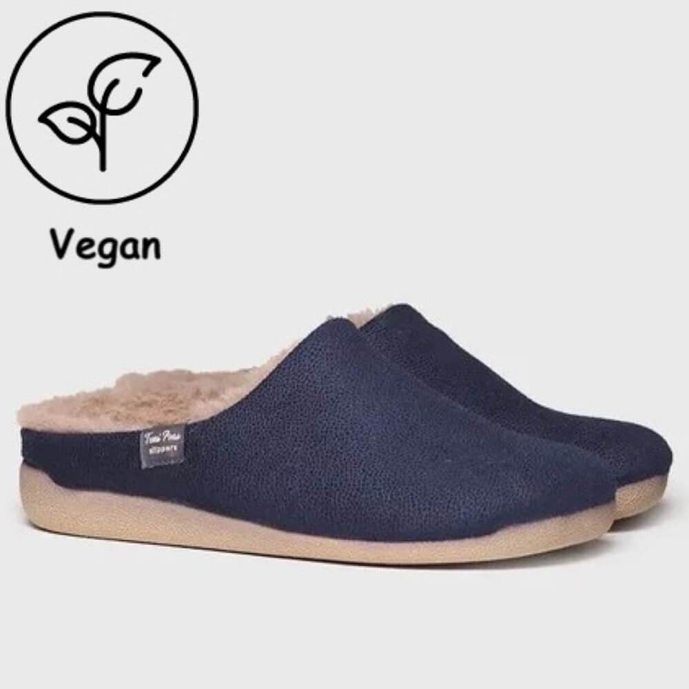 A pair of Toni Pons navy blue slip-on mule slippers with a soft beige sherpa lining and a light tan sole, shown on a light grey background with a 'Vegan' leaf icon overlay in the top-left corner.