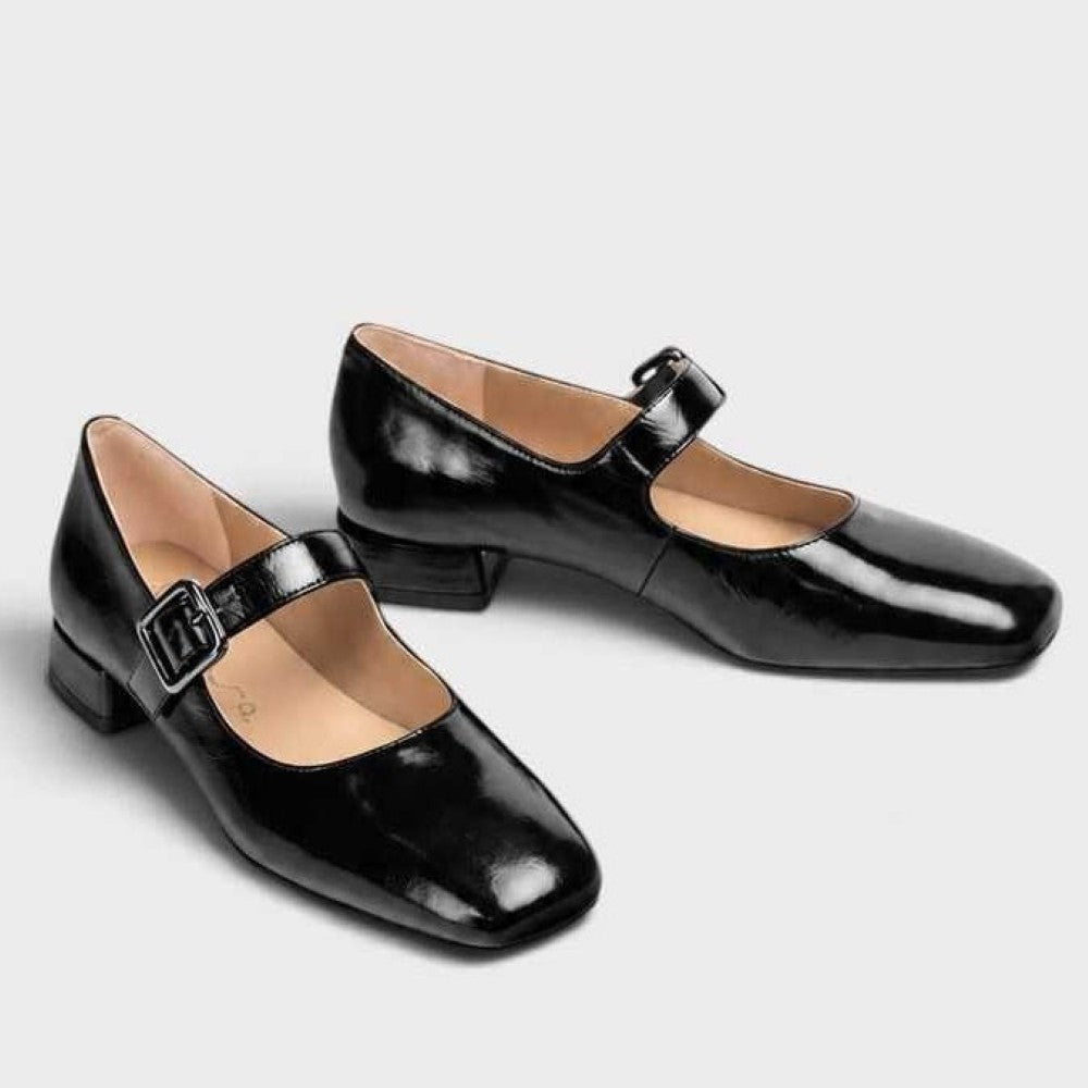A Pair of Unisa black patent leather Mary Jane flat shoes with a low block heel and a silver buckle strap, shown in profile against a light grey background.
