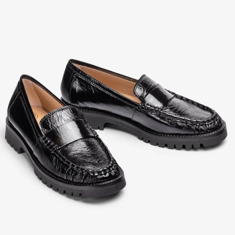 A pair of Unisa black leather penny loafers with a glossy, textured finish and chunky lug soles, displayed on a clean white background.