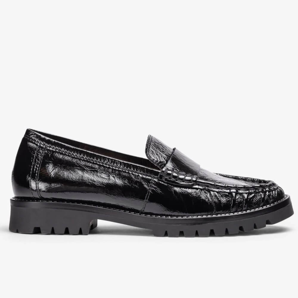 A Unisa black leather loafer with a textured, glossy finish and a chunky lug sole, shown in a side profile on a light grey background.