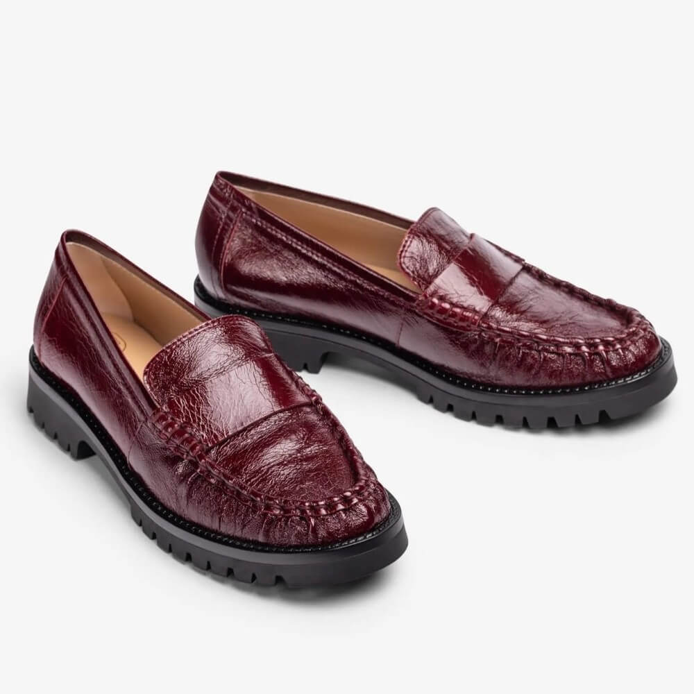 A pair of Unisa women's penny loafers in glossy burgundy leather with a textured crocodile pattern, featuring black lug soles and a tan interior, shown on a light grey background.
