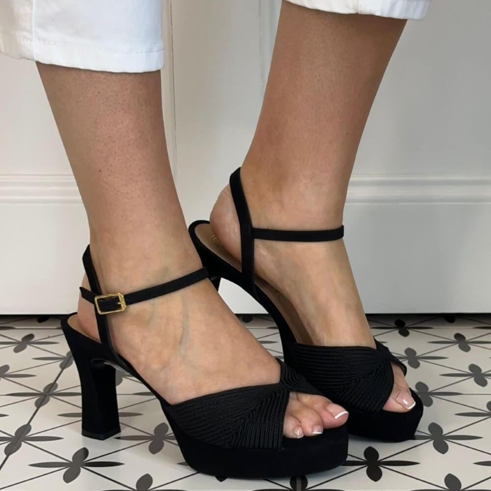 Unisa Black high-heeled sandals worn on a patterned floor.