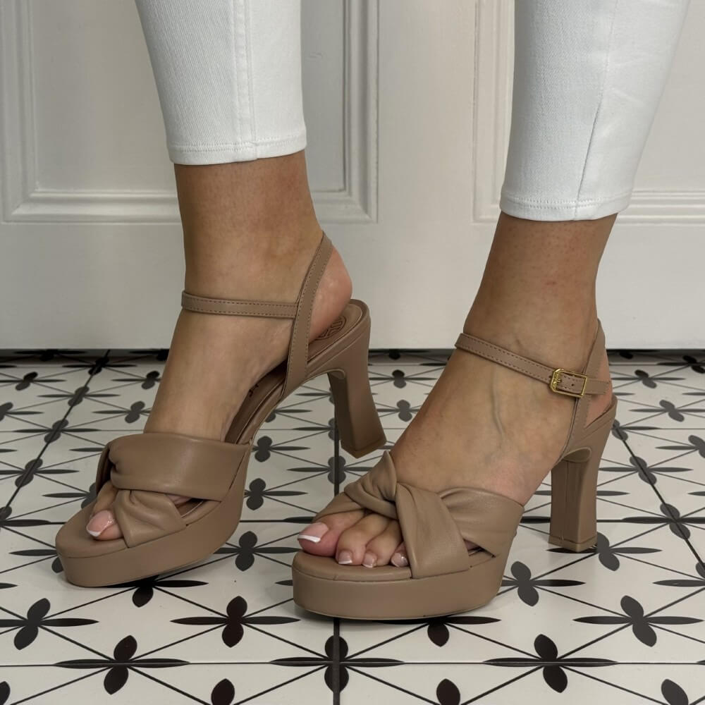 Beige platform sandals worn with white pants on a patterned floor.