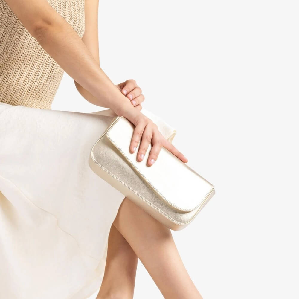 Woman holding a Unisa gold clutch bag on a plain background