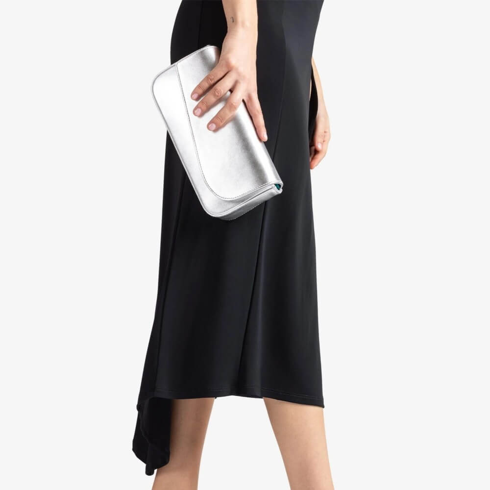 Person holding a silver clutch against a plain background