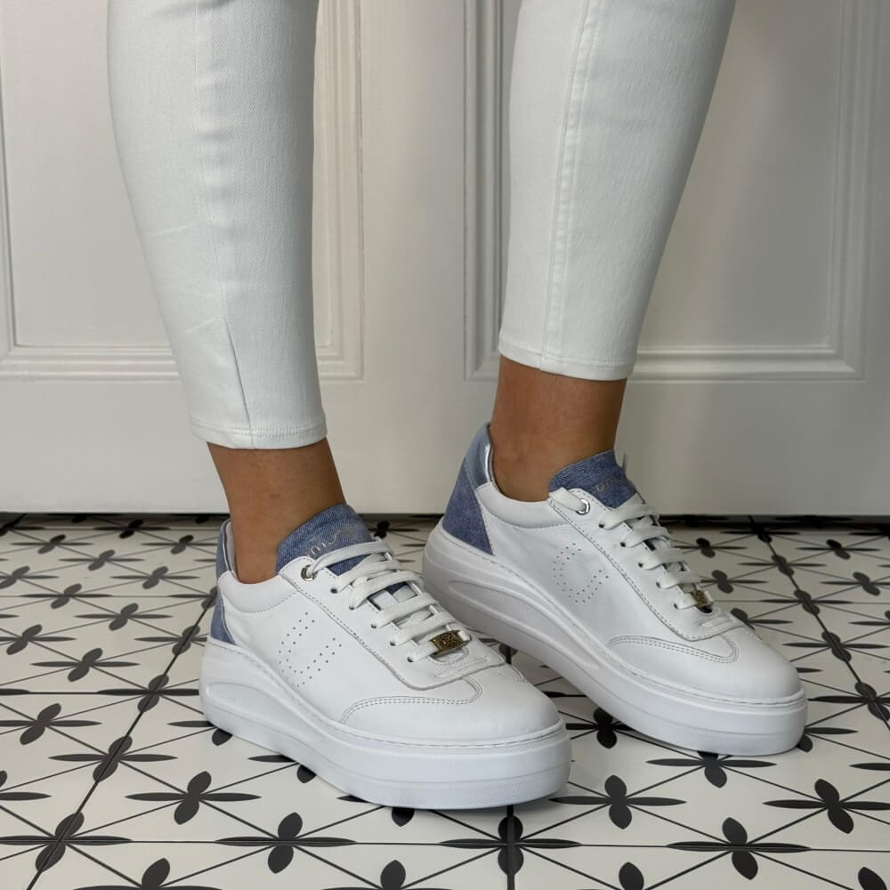 White sneakers with blue accents worn with white pants on a patterned floor.