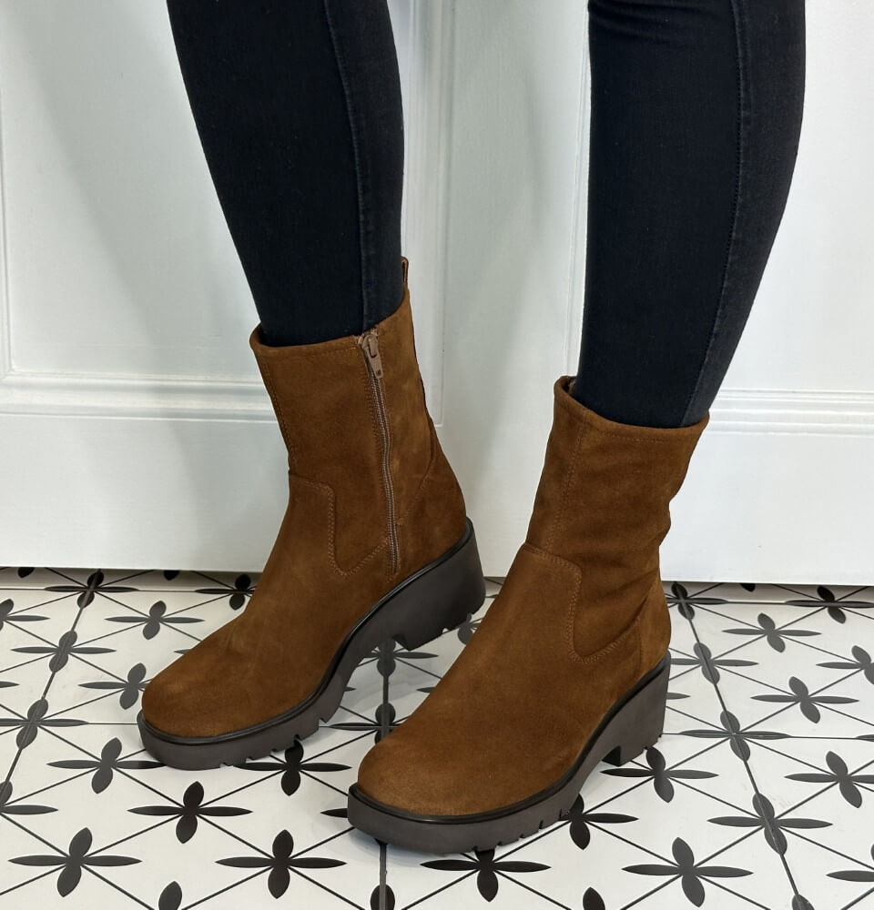 Brown ankle boots worn with black pants on a patterned floor.