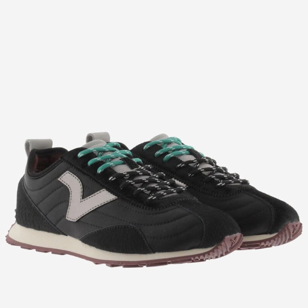 A black Victoria sneaker with a metallic silver V logo on the side, teal laces, and a cream midsole, shown against a light grey background.