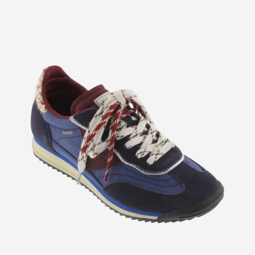A low-top sneaker by Victoria, featuring navy blue suede and synthetic panels, burgundy leather overlays, cream knit laces with red stripes, and a cream midsole on a light grey background.