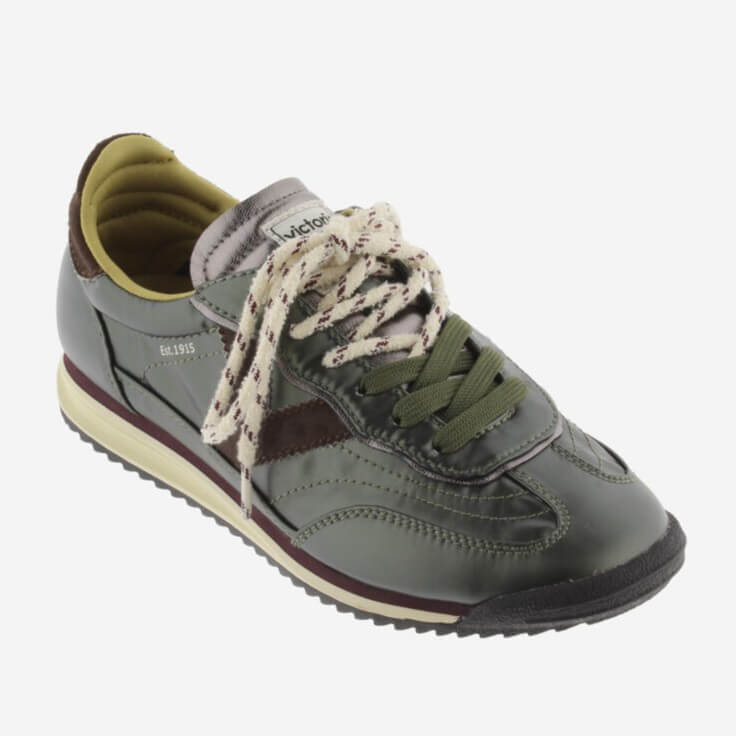 A Victoria low-top sneaker in dark olive green and brown with cream-colored laces and a cream midsole, shown from a side profile on a light grey background.