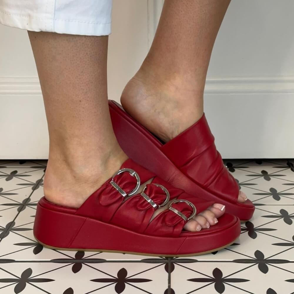 Marco Moreo Red platform sandals with a decorative buckle worn indoors on a patterned floor.