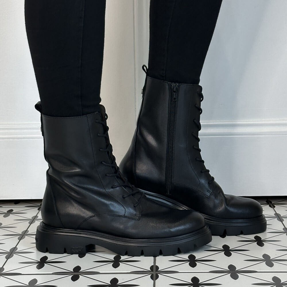 A pair of Wonders black leather lace-up ankle boots with side zippers, worn with black leggings on a black and white patterned tile floor.