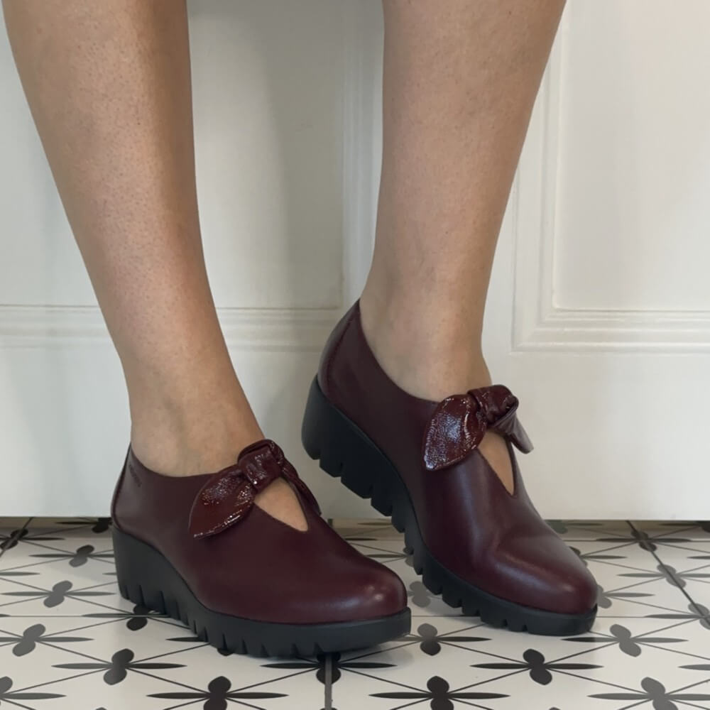 Wonders Wine leather slip-on with a patent bow trim worn on a tiled floor