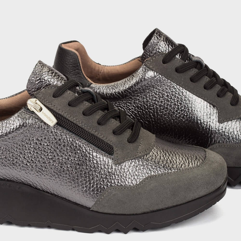 A pair of Wonders low-top sneakers in a mix of dark brown, grey, and metallic silver textures, featuring black laces and a chunky black sole, shown against a light grey background.