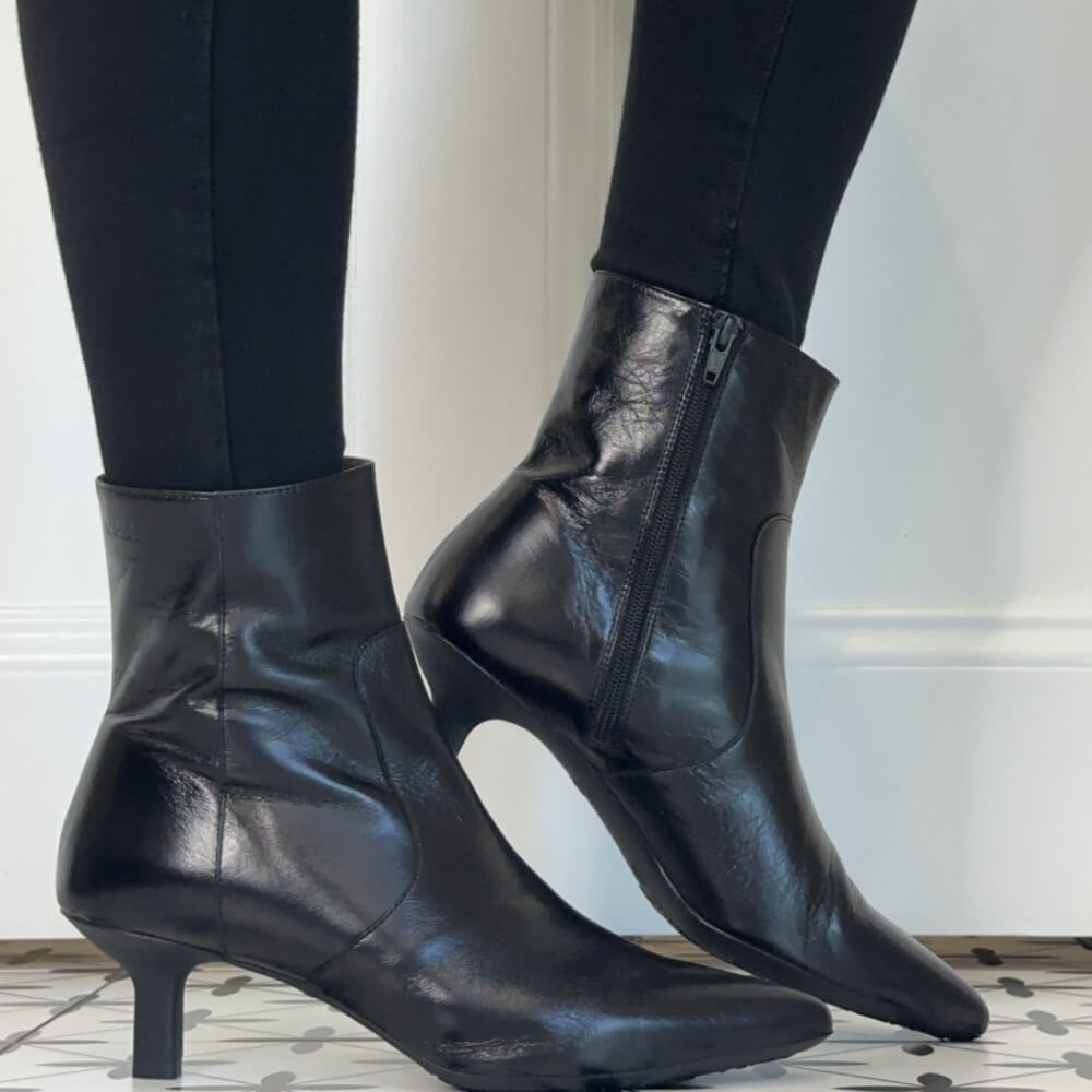 A pair of Wonders black leather ankle boots with kitten heels and side zippers, worn with black leggings.