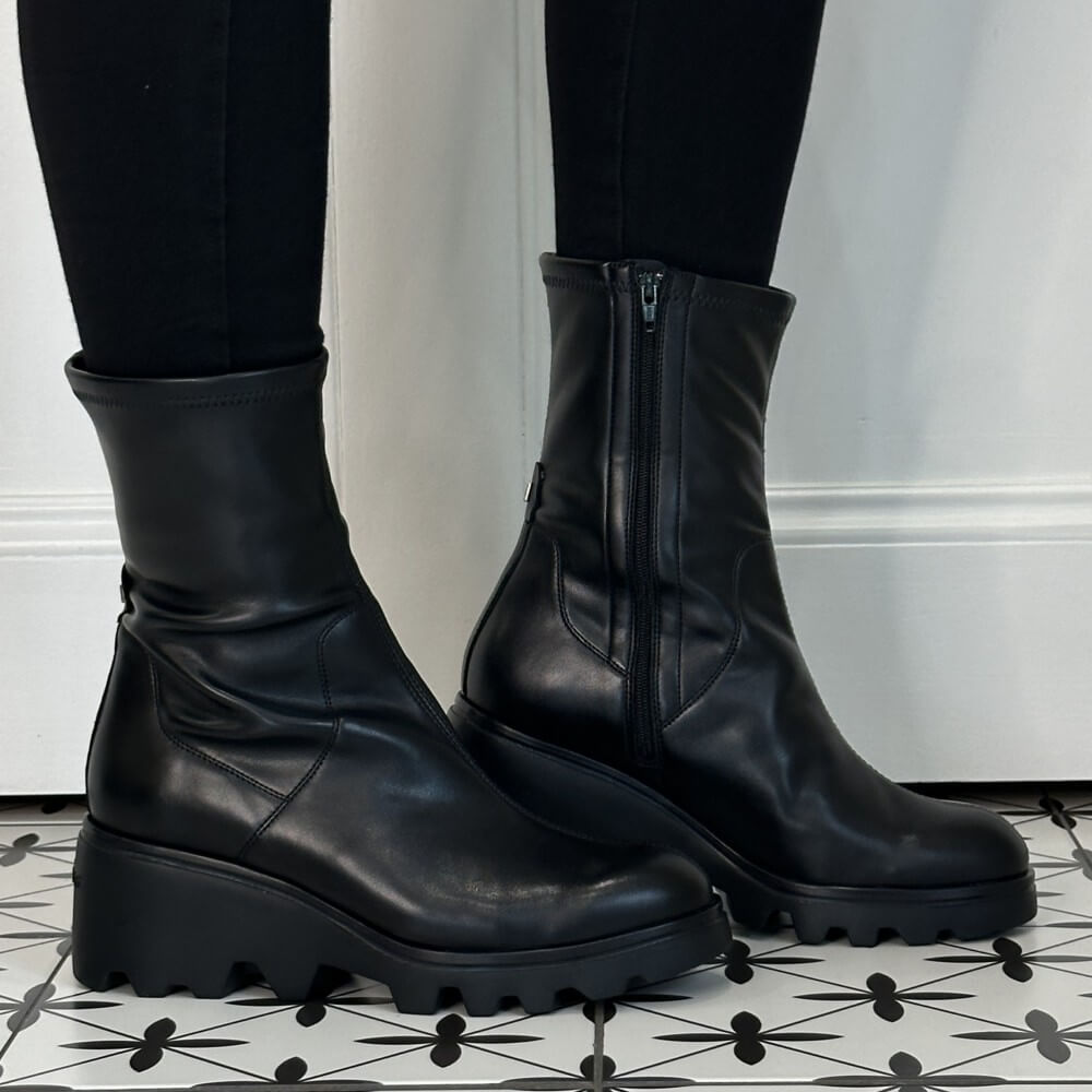 Wonders Black leather ankle boots with chunky wedge lug soles and side zippers, shown on a model wearing black leggings on a black and white patterned tile floor.