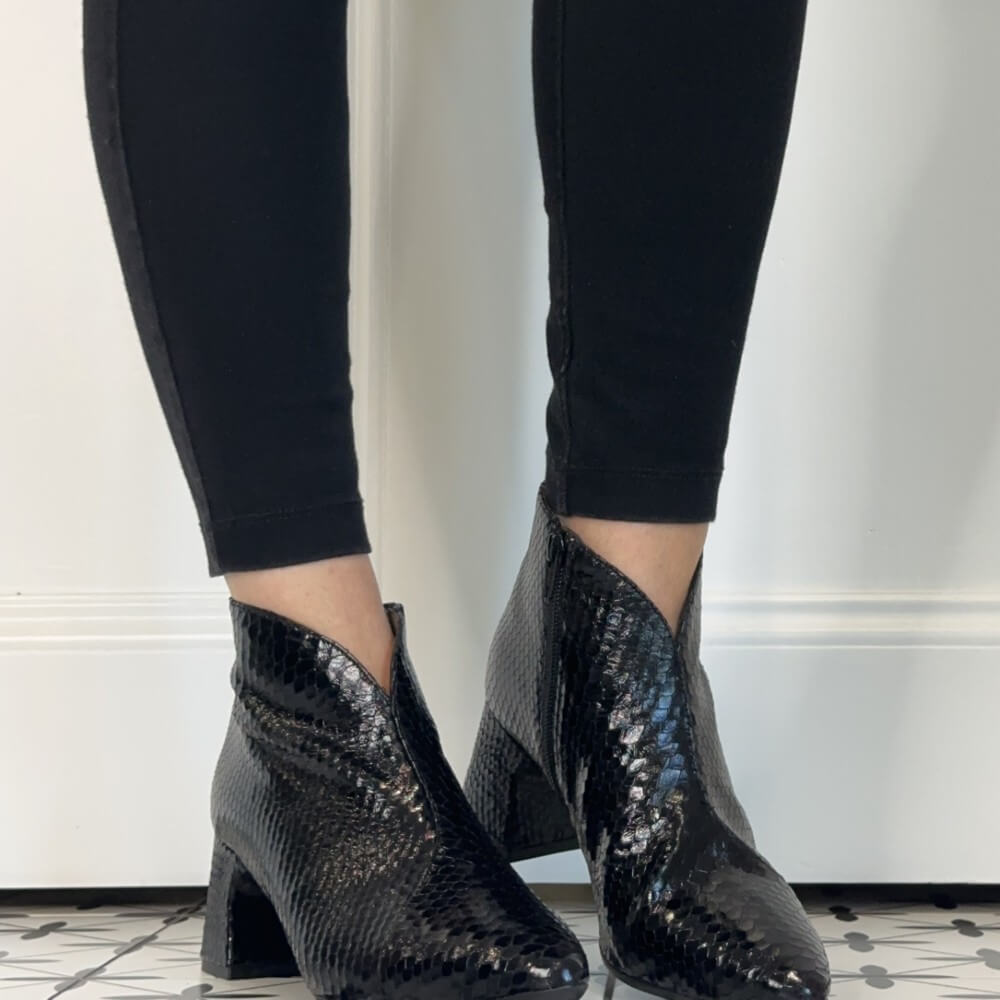 Wonders Black snakeskin-patterned ankle boots with block heels, shown on a model wearing black leggings against a white wall.