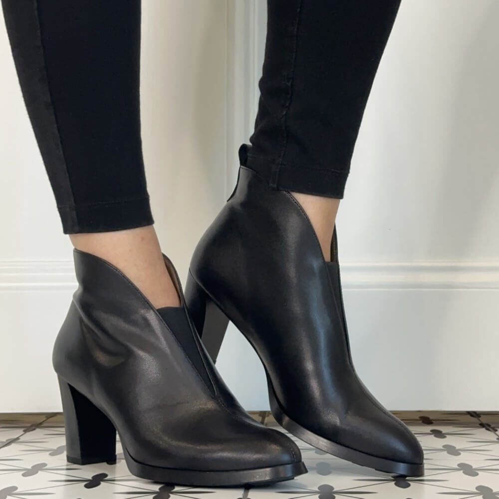 A pair of Wonders black leather ankle boots with a chunky block heel and pointed toe, shown on a model wearing black skinny jeans.