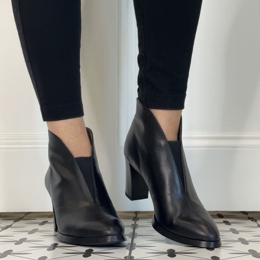 A pair of Wonders black leather ankle boots with a chunky block heel and pointed toe, shown on a model wearing black skinny jeans.