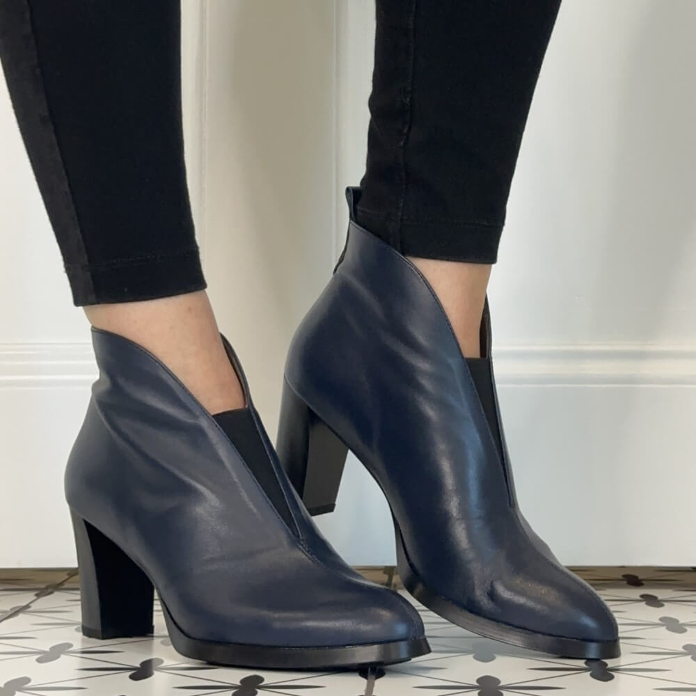 A pair of Wonders dark navy blue leather ankle boots with block heels, worn with black leggings on a patterned tile floor against a white wall.