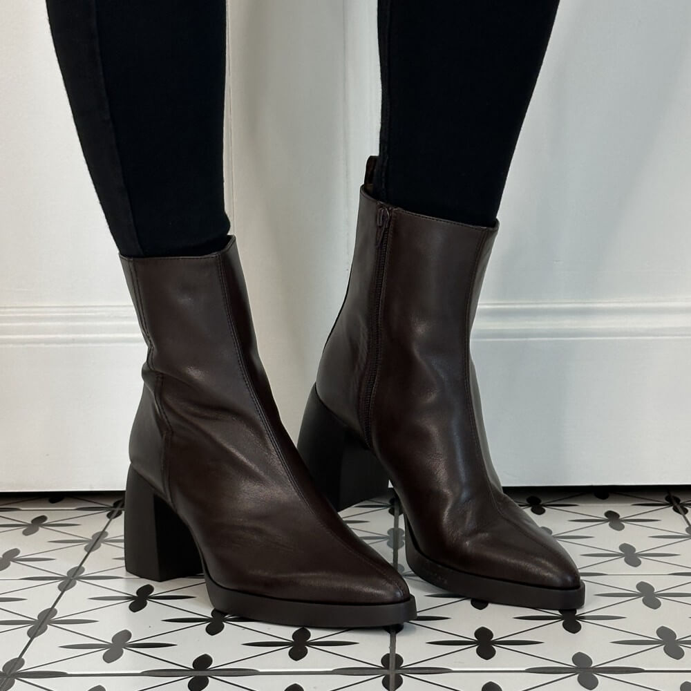 Wonders Dark brown leather ankle boots with block heels, shown on a model wearing black leggings against a white wall and patterned tile floor.