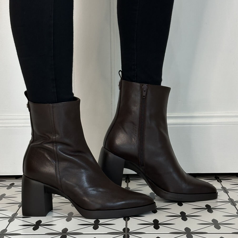 Wonders Dark brown leather ankle boots with block heels, shown on a model wearing black leggings against a white wall and patterned tile floor.
