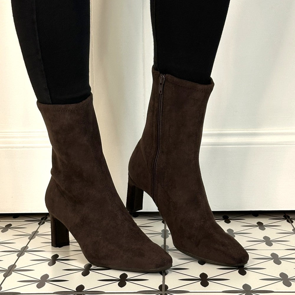 A pair of Wonders dark brown suede ankle boots with kitten heels, worn with black skinny jeans on a black and white patterned tile floor.