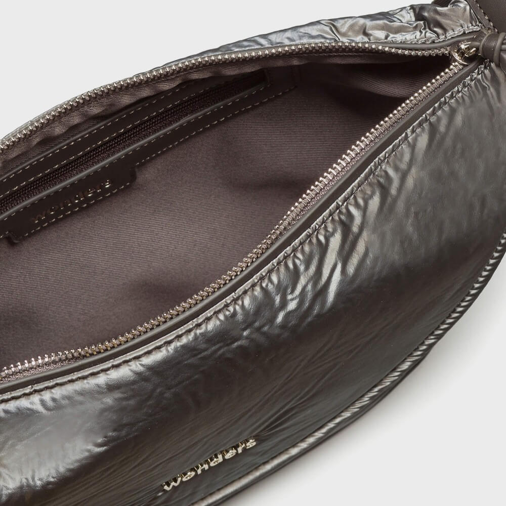 Close-up of an open metallic dark gray bag showing the interior lining and zipper, with a small gold-tone logo near the bottom edge.