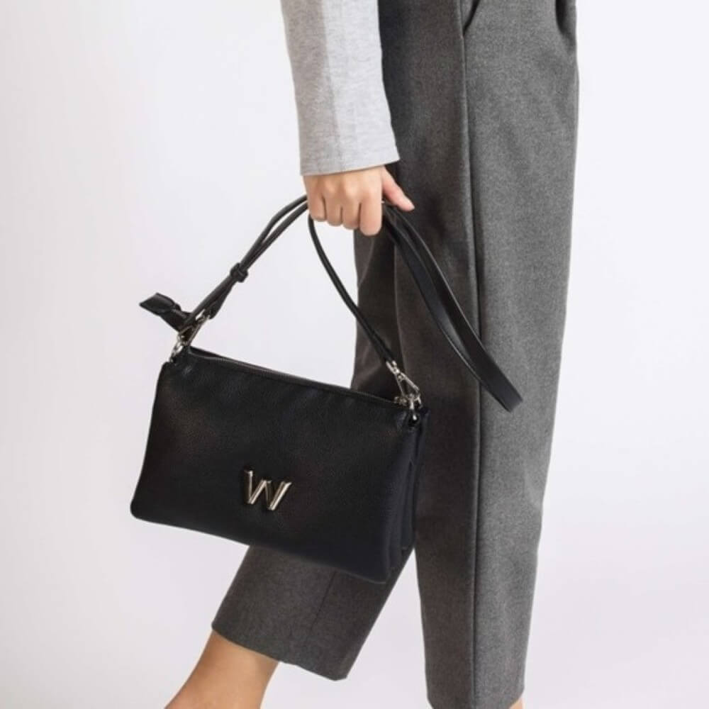 Person holding a black handbag with a W logo against a plain background