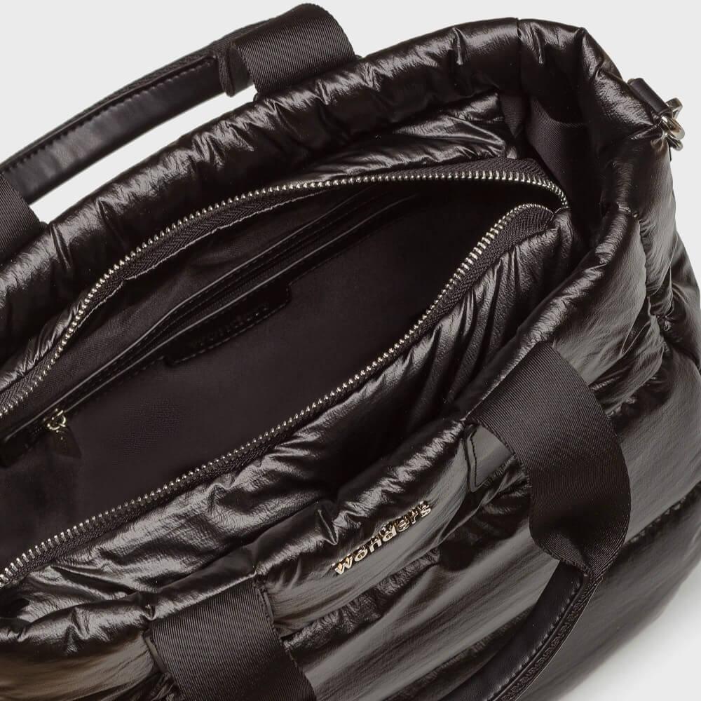 Close-up of the interior of a Wonders shiny black puffer bag, showing the zippered compartment, black fabric lining, and a small gold-tone brand logo on the side.