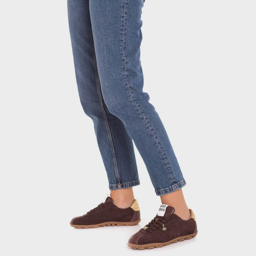 Person wearing blue jeans and brown shoes on a white background